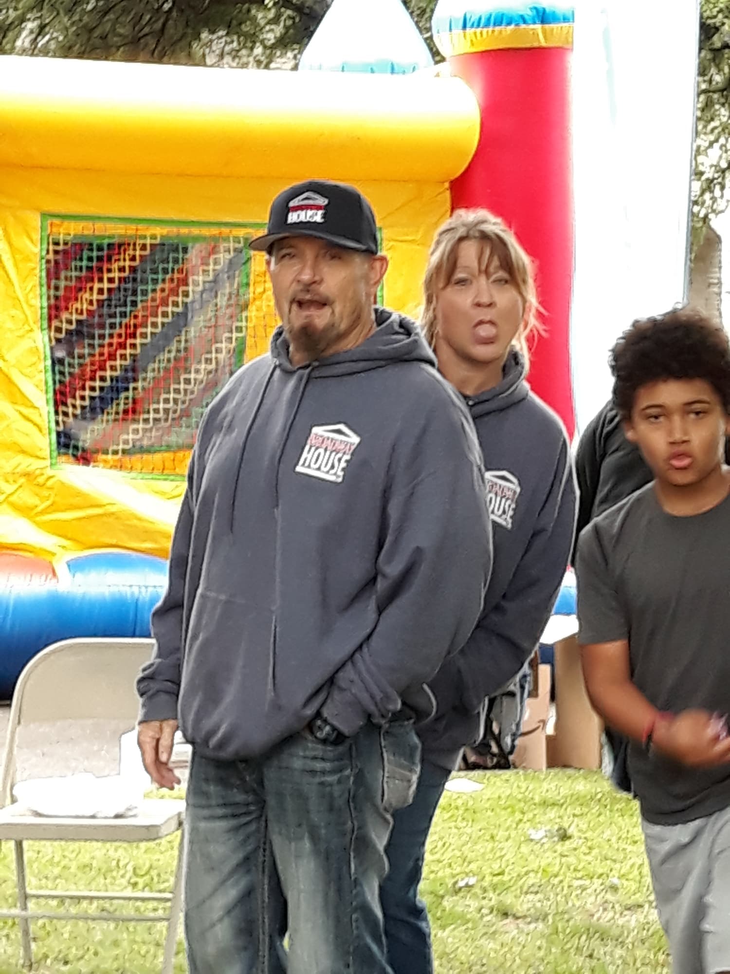 Two adults in Broadway House hoodies in front of a bounce house